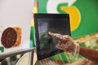 A hand using a till with the Subway logo in the background showing Subway® Franchisee Partners earnings